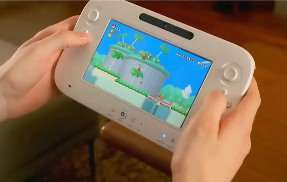 Hands hold a white gaming console with a colorful platform game on screen, featuring a character jumping across palm tree islands under a blue sky.
